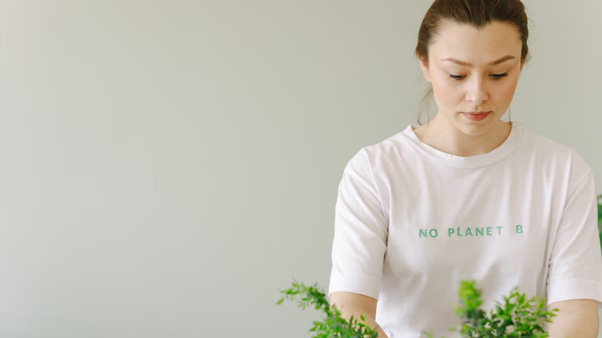 Young woman in 'No Planet B' shirt caring for indoor plants, promoting eco-consciousness.
